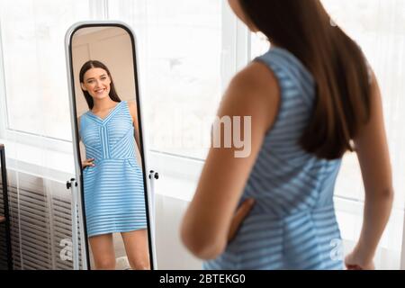 Ragazza in nuovo vestito guardando Specchio che posa a casa Foto Stock