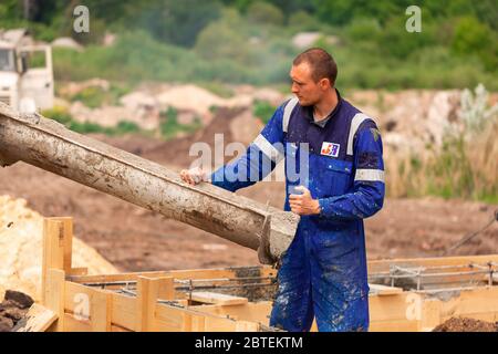 Lavoratore di costruzione che posa cemento o calcestruzzo nella cassaforma di fondazione. Costruzione di fondamenta di casa Foto Stock