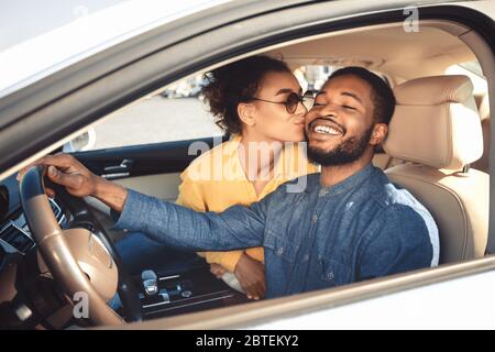 Moglie nera Kissing marito felice seduto in Nuova Auto di Lusso Foto Stock