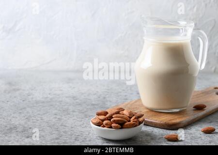 Latte di mandorle in caraffa di vetro e noci su tavola grigia. Primo piano. Alimentazione vegana sana. Mancanza di colesterolo. Spazio per il testo. Foto Stock