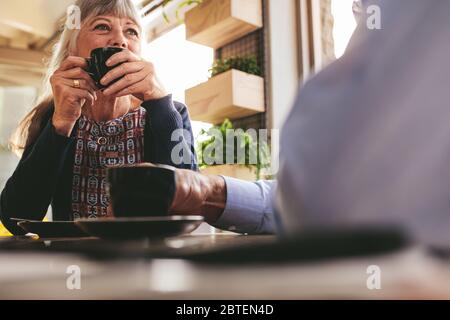 Donna matura seduta al caffè bevendo una tazza di caffè e parlando con suo marito. Coppia senior che ha parlato mentre beve caffè in un caffè Foto Stock