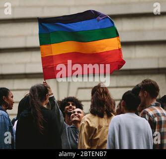 La gente partecipa alla sfilata annuale del Pride e alle celebrazioni in città. Giovane donna che sventolava bandiera gay arcobaleno con persone in piedi intorno. Foto Stock