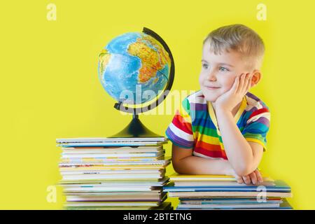 Il ragazzo si siede accanto ai libri per bambini e al globo. Sfondo verde. Foto Stock