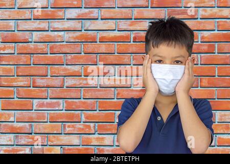 La mano che tiene la maschera sul fondo asiatico ragazzo muro di mattoni. Foto Stock