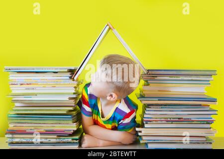 Il bambino si siede all'interno di una casa fatta di libri per bambini. Sfondo verde. Molti libri. Foto Stock