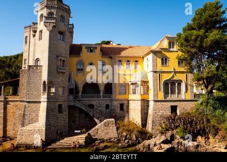 Europa, Portogallo, caisca. Il Palácio dos Condes de Castro Guimarães illuminato dal sole con i turisti che nuotano in acqua ai piedi del s. Foto Stock