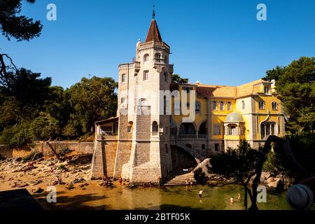 Europa, Portogallo, caisca. Il Palácio dos Condes de Castro Guimarães illuminato dal sole con i turisti che nuotano in acqua ai piedi del s. Foto Stock