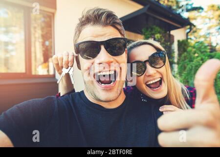 giovane coppia felice con le chiavi in mano in piedi fuori della loro nuova casa e prendere un selfie Foto Stock