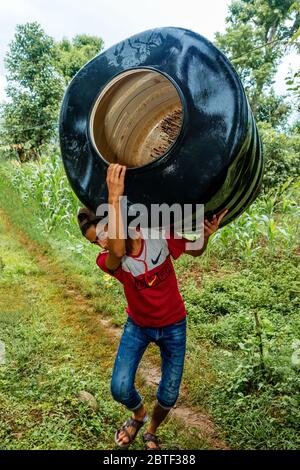 Gorkha, Nepal - Giugno 26,2019: Piccolo ragazzo Nepalese che porta un tamburo pesante sulla sua spalla, trasportando carichi pesanti Foto Stock