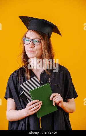 Ragazza in abito accademico e con un diploma in mano su uno sfondo giallo Foto Stock