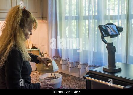 Donna adulta che si filma preparando l'impasto con un mixer per una torta durante la quarantena. Foto Stock