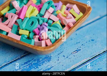 lettere colorate in legno in una ciotola su sfondo blu con spazio per la copia Foto Stock