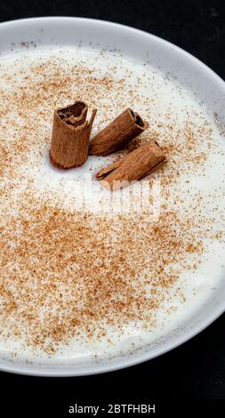 Latte di riso con cannella, piatto bianco su fondo nero Foto Stock