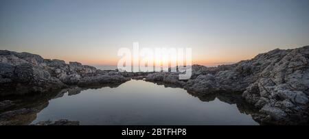 Tramonto su una spiaggia rocciosa con riflessi d'acqua Foto Stock