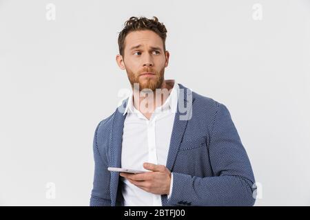 Immagine di un uomo confuso che indossa una giacca che digita sullo smartphone isolato su sfondo bianco Foto Stock