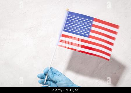 Mano in guanto di protezione che tiene la bandiera americana contro sfondo testurizzato bianco. 4 luglio concetto. Spazio di copia Foto Stock