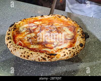 Pizza italiana appena cotta con brigio, pomodori e carne su pala, foto mobile Foto Stock
