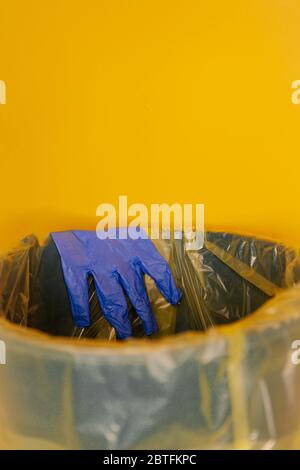 Gettare il guanto monouso nel contenitore su fondo arancione isolato. Concetto di Coronovirus. Foto Stock