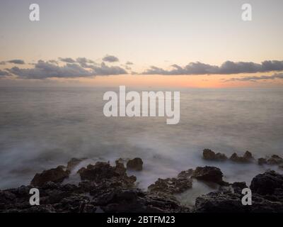 Tramonto con onde che si infrangono sulla costa rocciosa Foto Stock
