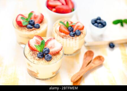 In casa, squisiti dessert Tiramisu' in vetri decorati con fragola, mirtillo, menta bianca sul tavolo di legno, Foto Stock