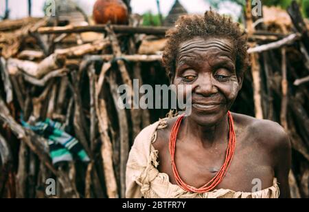 TRIBÙ TOPOSA, SUD SUDAN - 12 MARZO 2020: Vecchia donna cieca di Toposa Tribe in piedi su sfondo offuscato di capanna bastone nel villaggio nel Sudan del Sud Foto Stock