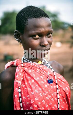 TOPOSA TRIBE, SUD SUDAN - 12 MARZO 2020: Adolescente con capelli corti indossando abiti e accessori luminosi e guardando la fotocamera su sfocato Foto Stock