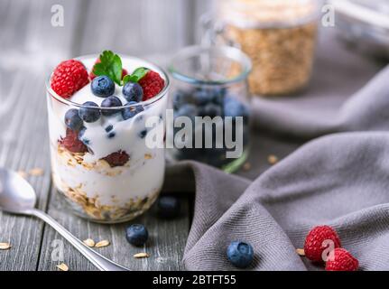 Yogurt bianco in vaso di vetro con lamponi e mirtilli su tovagliolo grigio. Foto Stock