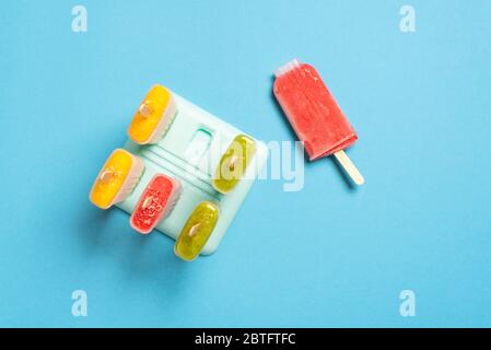 Gelati nelle muffe del papsiclo su un tavolo blu, vista dall'alto. Gelato fatto in casa con frutta fresca. Dessert estivo a base di ingredienti vegani Foto Stock