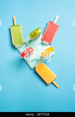 Gelato fatto in casa nelle loro forme di plastica su sfondo blu, vista dall'alto. Gelato a base di frutta fresca. Foto Stock