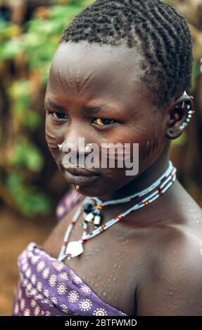 TRIBÙ TOPOSA, SUD SUDAN - 12 MARZO 2020: Ragazza adolescente con viso scarrito e accessori tradizionali che si affaccia mentre si vive nel villaggio di Toposa Foto Stock
