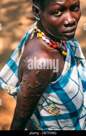 TRIBÙ BOYA, SUD SUDAN - 10 MARZO 2020: Donna in accessori colorati tradizionali e stoffa a scacchi con piercing rituale e cicatrici che guardano Foto Stock