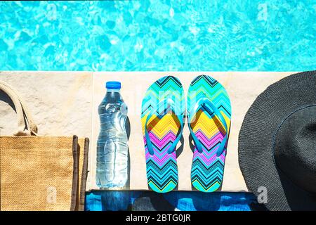 La piscina e il cappello di paglia, colorato flip flop, borsa di vimini, cappello di paglia, bottiglia con acqua ancora come sunny estate sfondo. Vacanze viaggi abbronzatura di Concetto di vacanza. Appartamento laico, vista dall'alto, vicino. Foto Stock