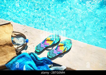 La piscina e il cappello di paglia, colorato flip flop, borsa di vimini, cappello di paglia, bottiglia con acqua ancora come sunny estate sfondo. Vacanze viaggi abbronzatura di Concetto di vacanza. Appartamento laico, vista dall'alto, vicino. Foto Stock