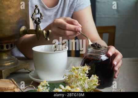 Vista laterale delle mani femminili mette marmellata fatta in casa in tazza di tè da samovar, concetto di festa del tè Foto Stock