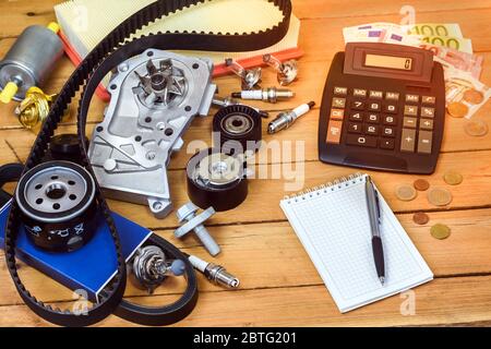 Varie parti di auto con calcolatrice, soldi, un blocco e una matita a sfera sul tavolo di legno. Foto Stock