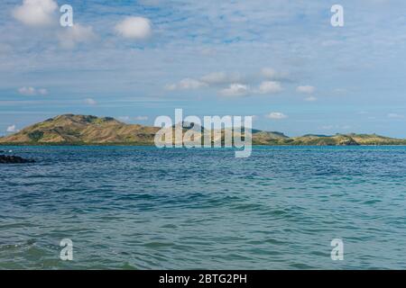 Ampia vista angolare di un'isola tropicale collinare sull'orizzonte blu dell'acqua e un cielo blu. Isola di Nacula delle isole Yasawa nelle Figi Foto Stock