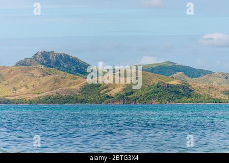 Ampia vista angolare di un'isola tropicale collinare sull'orizzonte blu dell'acqua e un cielo blu. Isola di Nacula delle isole Yasawa nelle Figi Foto Stock