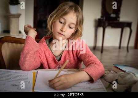 ragazza blonde lefthanted che scrivono i compiti durante le restrizioni di blocco del virus corona Foto Stock