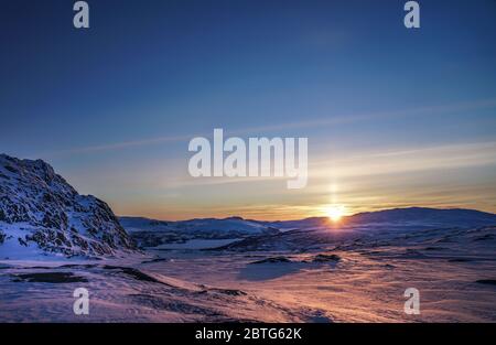 Tramonto molto bello sulle montagne scandinave - raggi di sole rosso arancio che colorano la neve bianca e il cielo blu Foto Stock