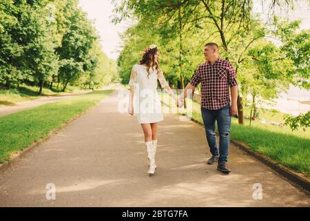 La ragazza incinta e suo marito sono felici di tenere le mani, va all'aperto sullo sfondo del giardino con gli alberi. Primo piano. Metà superiore. Guardate ogni altra Foto Stock