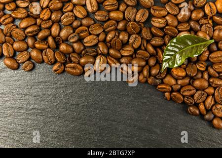 Chicchi di caffè su sfondo nero. Concetto java stimolante e fluido. Chicchi di caffè con foglie. Foto Stock