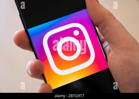 Una mano di un uomo che tiene uno smartphone con un grande logo per l'app di social media per la condivisione di foto Instagram Foto Stock