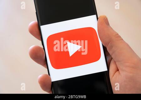 Una mano di un uomo che tiene uno smartphone con un grande logo per l'applicazione YouTube, l'app per la condivisione di video sui social media Foto Stock