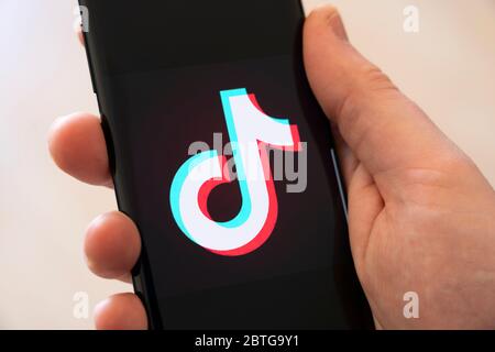 Una mano di un uomo che tiene uno smartphone con un grande logo per l'app cinese di social media per la condivisione di video Tik Tok Foto Stock