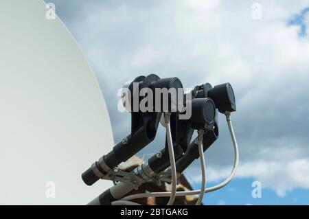 Antenna parabolica offset con tre convertitori su sfondo cielo nuvoloso. Tre convertitori neri con cavo e parte dell'antenna da vicino Foto Stock