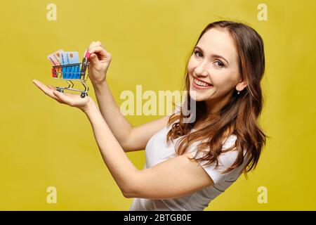 Bella ragazza in abiti casual tiene un carrello di shopping nel palmo della sua mano con carte di credito bancario. Foto Stock