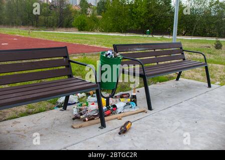 Mosca, Russia - 05/20/2020 - due panchine e un sacco di rifiuti vicino al cestino pieno. Strade e parchi sporchi senza pulizia Foto Stock