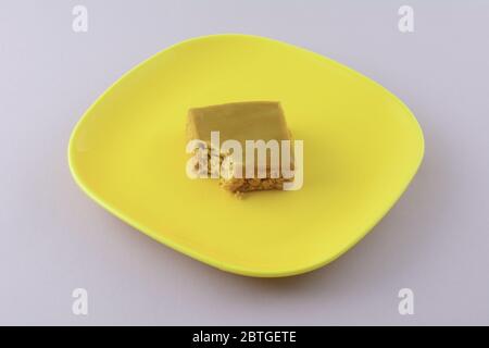 Tofee flapjack squadrate cake bar con morso mancante sul piatto giallo su sfondo lavanda Foto Stock