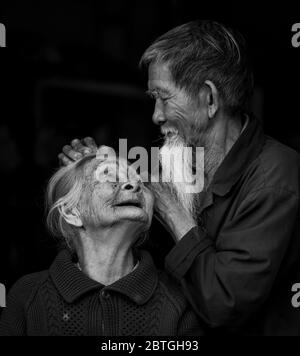 HOI AN - 10 MARZO 2018: Un vecchio che fissa delicatamente i capelli della moglie su uno sfondo nero a Hoi An, Vietnam, il 10 marzo 2018 Foto Stock