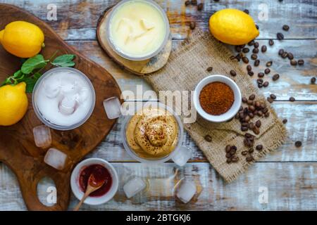 Il caffè Dalgona e altre bevande fredde sono disposti a caso insieme ad alcuni ingredienti di base, come i chicchi di caffè, i limoni, le marmellate, i cubetti di ghiaccio e lo zucchero. Foto Stock